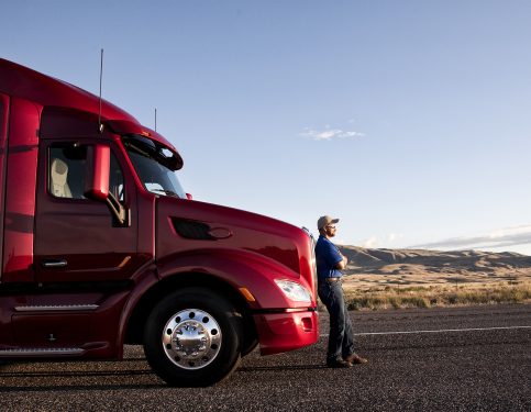 Truck driver leaning on the grill of his commercial truck.